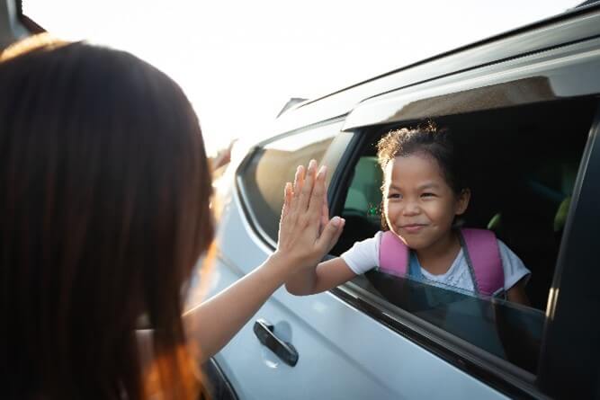 A mother high-fives a child as she is heading off to school.