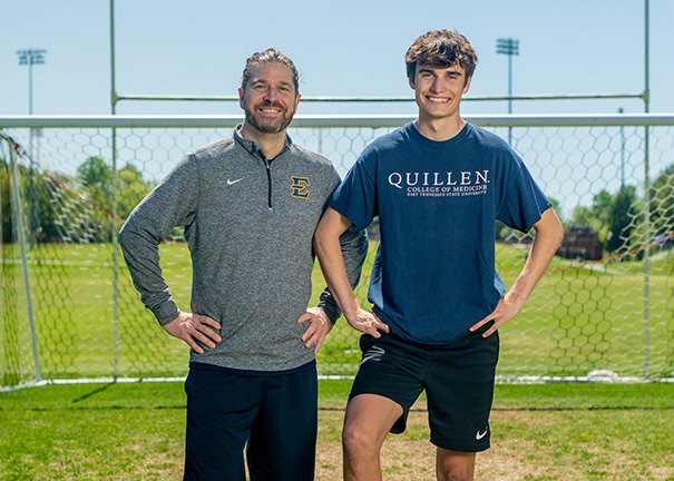 Father and son posing in front of soccer goal.