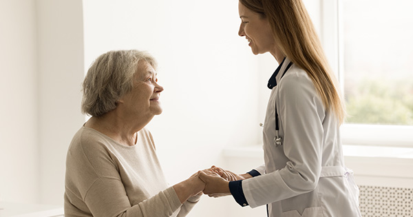 Health care provider dressed in a white coat comforts a patient by holding their hands.