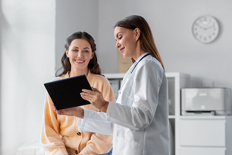 Provider holding tablet explaining something to smiling patient in a clinic room.