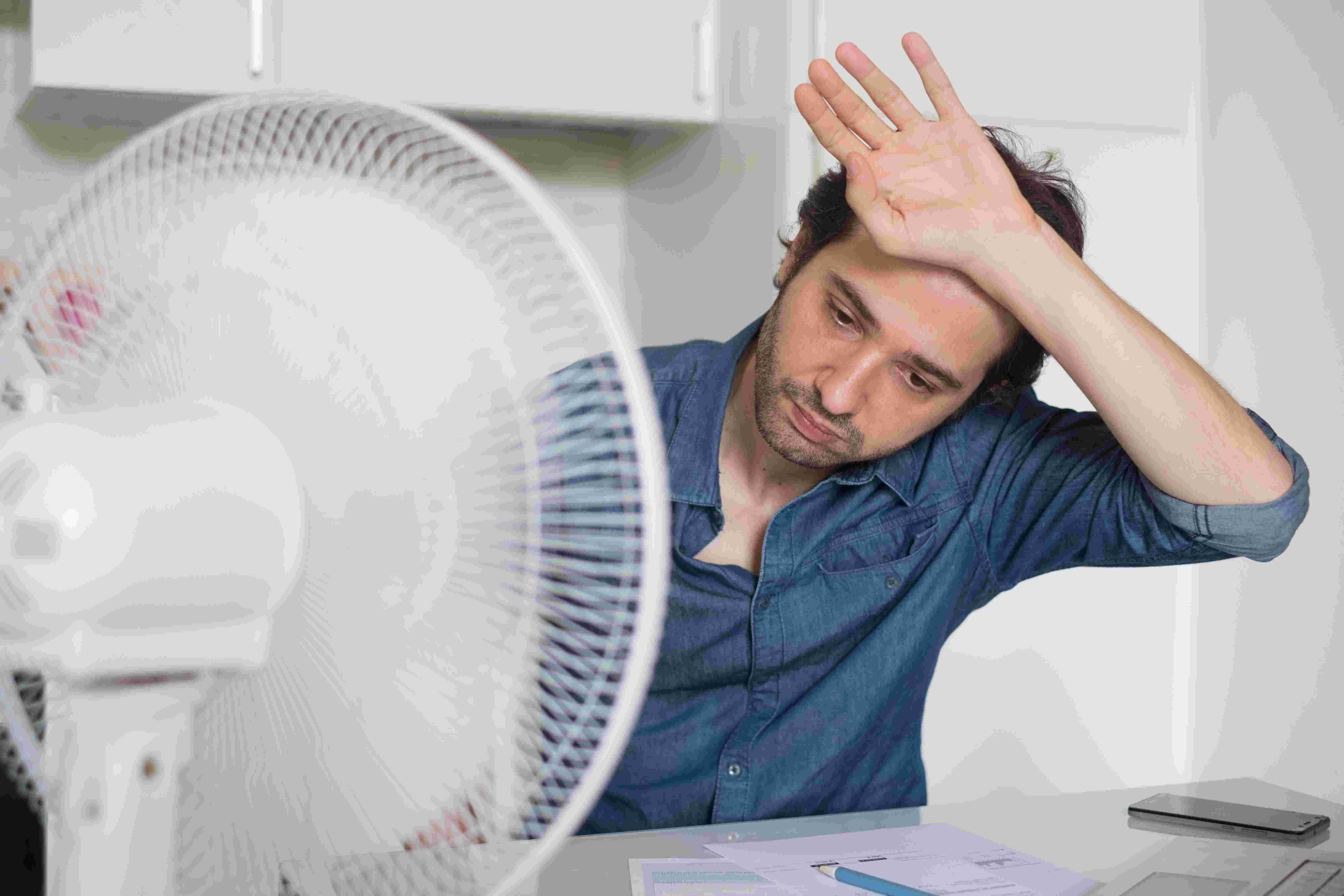 overheated man sits in front of a fan